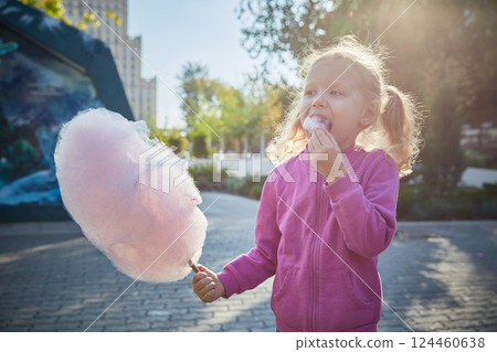 Curly-haired girl enthusiastically eats cotton candy. The concept of a family of children and happiness with children. Curly-haired girl enthusiastically eats cotton candy. The concept of a family of children and happiness with children. 124460638