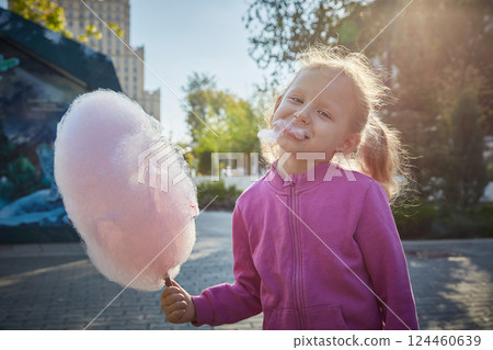 Curly-haired girl enthusiastically eats cotton candy. The concept of a family of children and happiness with children. Curly-haired girl enthusiastically eats cotton candy. The concept of a family of children and happiness with children. 124460639