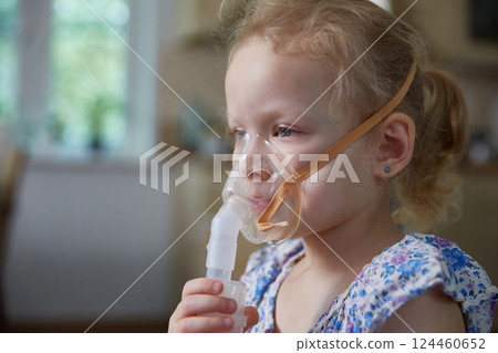 Sick little girl making inhalation with nebulizer to reduce coughing at home, child taking medication while breathing in through face mask. Bronchitis and asthma treatments for children. 124460652
