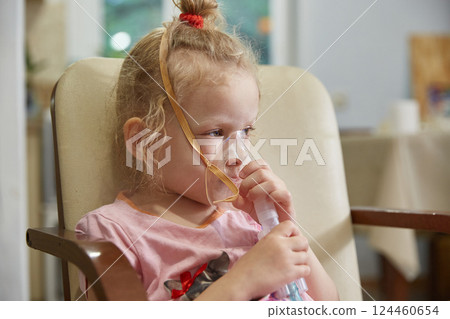 A sick girl breathes with a nebulizer inhaler at home during her illness. Lifestyle. 124460654