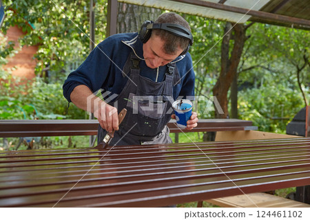 A man in a work suit paints metal pipes. A man in a work suit paints metal pipes. 124461102