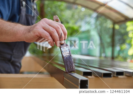 A man's hand paints metal square pipes with a primer on metal. Copy space. 124461104
