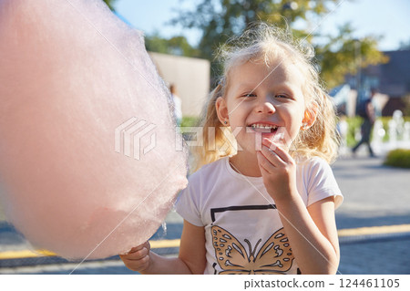 a girl-child in an amusement park eats cotton candy in the summer. The concept of happiness, relaxation, summer holidays and school holidays. a girl-child in an amusement park eats cotton candy in the summer. The concept of happiness, relaxation, summer holidays and school holidays. 124461105
