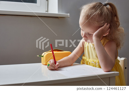 A bored girl draws with pencils at table at home. A bored girl draws with pencils at table at home. 124461127