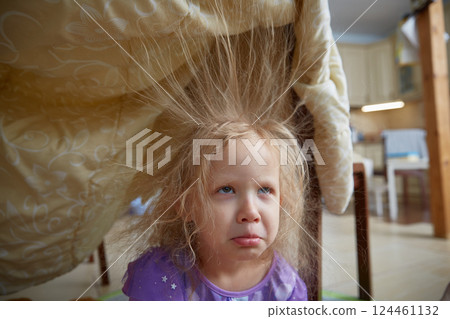 Sad girl is sitting at home with electrified hair sticking up. Children's games for preschoolers at home. Sad girl is sitting at home with electrified hair sticking up. Children's games for preschoolers at home. 124461132