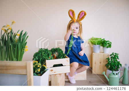 Cute little child girl wearing bunny ears on Easter day and holding carrot in hand 124461176