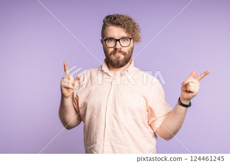Young man pointing fingers in opposite directions with serious face. Decision making, options, and visual emphasis on choice Young man pointing fingers in opposite directions with serious face. Decision making, options, and visual emphasis on choice 124461245