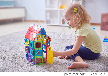 A curly-haired child collects a house made of colored designer parts on the carpet. Copy space A curly-haired child collects a house made of colored designer parts on the carpet. Copy space 124461264