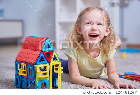 Cheerful girl laughs lies on the carpet next to the toy house Cheerful girl laughs lies on the carpet next to the toy house 124461267