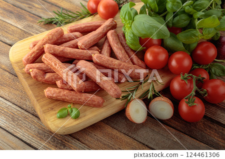Sausages with basil and tomatoes on a cutting board. 124461306