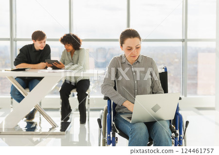 Accessible environment. Woman in chair for people with disability working with laptop in modern office. Diverse multiracial group of people colleagues working together. Young professional team Accessible environment. Woman in chair for people with disability working with laptop in modern office. Diverse multiracial group of people colleagues working together. Young professional team 124461757
