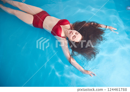 A young woman enjoys relaxing in a swimming pool or a bath with salt water. A brunette with loose hair is relaxing in a spa salon. Top view. Copy space. 124461788