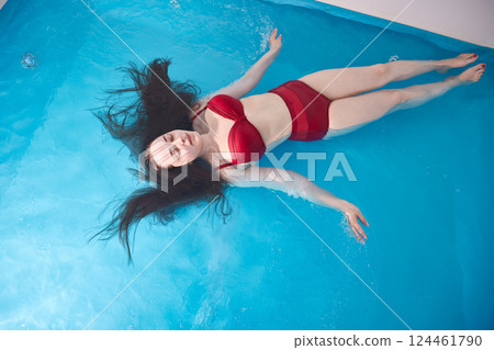 A young woman enjoys relaxing in a swimming pool or a bath with salt water. A brunette with loose hair is relaxing in a spa salon. Top view. Copy space. 124461790