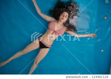 Top view of an attractive young woman floating on blue water. Relaxation and spa therapy. Copy Space 124462126