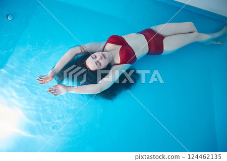 A young woman enjoys relaxing in a swimming pool or a bath with salt water. A brunette with loose hair is relaxing in a spa salon. Top view. Copy Space. A young woman enjoys relaxing in a swimming pool or a bath with salt water. A brunette with loose hair is relaxing in a spa salon. Top view. Copy Space. 124462135