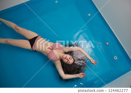 Top view of an attractive young woman floating on blue water. Relaxation and spa therapy. Top view. Copy Space 124462277