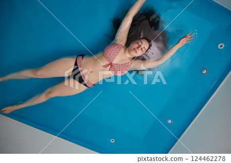 A young girl enjoys relaxing in a pool with concentrated sea water. Floating. Top view. Copy space 124462278