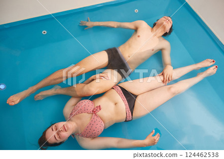Man and a woman lie relaxed in a therapeutic wellness pool with salt water. Top view Man and a woman lie relaxed in a therapeutic wellness pool with salt water. Top view 124462538
