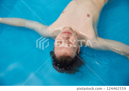 Man is swimming in the pool on his back with his arms spread wide. Wellness, relaxation and spa therapy. Copy space. Man is swimming in the pool on his back with his arms spread wide. Wellness, relaxation and spa therapy. Copy space. 124462559