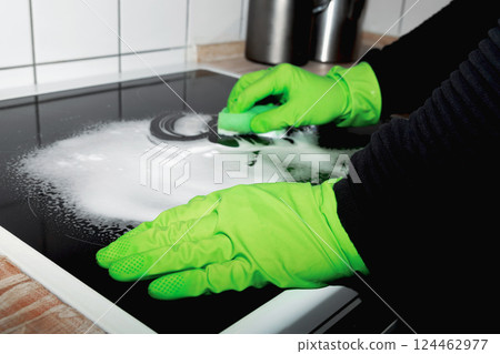 A man wearing cleaning gloves wipes the induction hob. A man wearing cleaning gloves wipes the induction hob. 124462977
