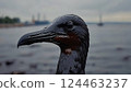 A seabird covered in thick black oil struggling to move on a polluted shoreline, its feathers drenched and sticky, with a dark, oily ocean in the background 124463237