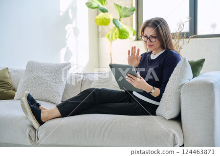 Middle aged woman sitting at home on sofa using digital tablet for video call, chat Middle aged woman sitting at home on sofa using digital tablet for video call, chat 124463871