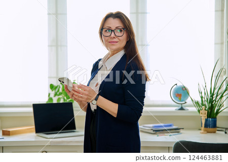 Middle aged smiling businesswoman with smartphone in home office 124463881