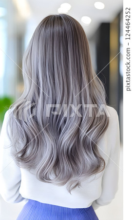 Long wavy silver hair flowing gracefully down a womans back in a brightly lit modern interior with soft ambiance 124464252