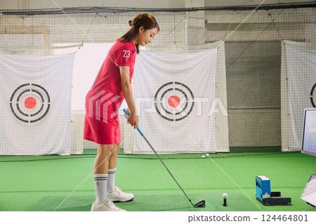 A woman practicing at an indoor golf driving range A woman practicing at an indoor golf driving range 124464801