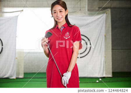 A woman practicing at an indoor golf driving range 124464824