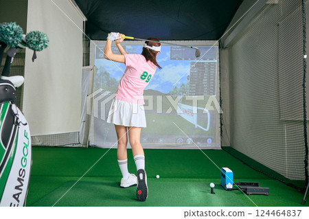 A woman practicing at an indoor golf driving range 124464837