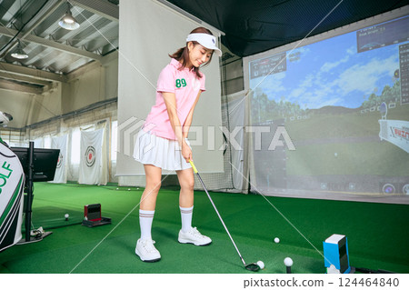 A woman practicing at an indoor golf driving range 124464840
