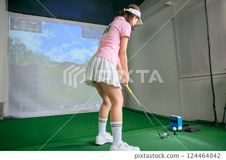 A woman practicing at an indoor golf driving range A woman practicing at an indoor golf driving range 124464842