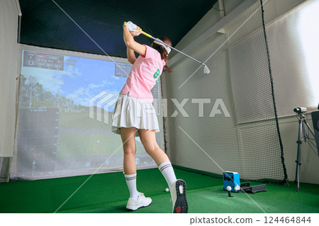 A woman practicing at an indoor golf driving range A woman practicing at an indoor golf driving range 124464844
