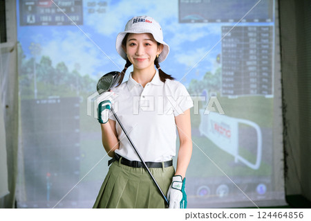 A woman practicing at an indoor golf driving range 124464856