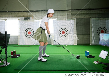 A woman practicing at an indoor golf driving range A woman practicing at an indoor golf driving range 124464875