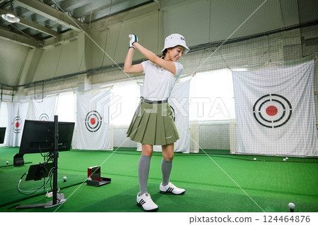 A woman practicing at an indoor golf driving range 124464876