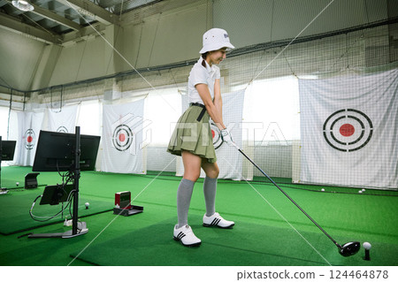 A woman practicing at an indoor golf driving range 124464878