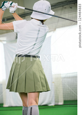 A woman practicing at an indoor golf driving range A woman practicing at an indoor golf driving range 124464883
