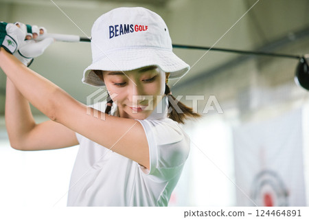A woman practicing at an indoor golf driving range 124464891