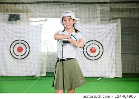 A woman practicing at an indoor golf driving range 124464900