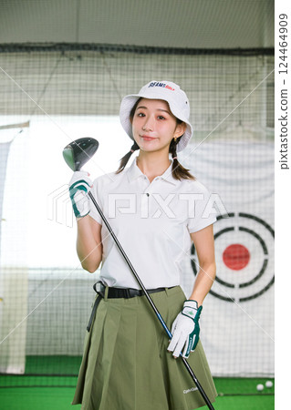 A woman practicing at an indoor golf driving range 124464909