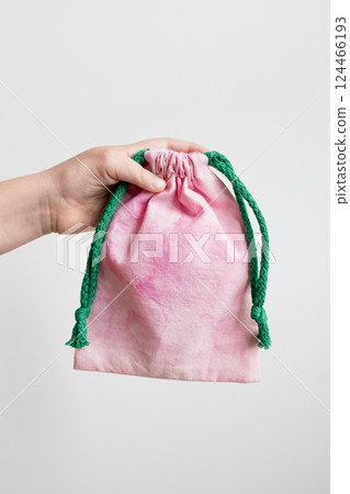 Hand holding pink drawstring bag with green rope against white background Hand holding pink drawstring bag with green rope against white background 124466193