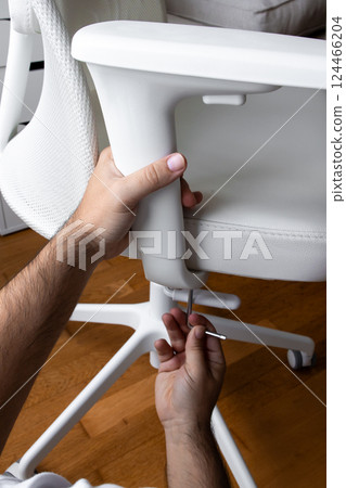Male assembling white office chair with allen wrench on wooden floor 124466204