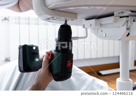 Male adult assembling furniture with electric drill indoors Male adult assembling furniture with electric drill indoors 124466218