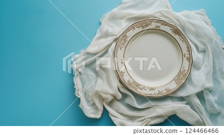 A decorative porcelain plate with golden floral rim on white cloth over a blue surface 124466466
