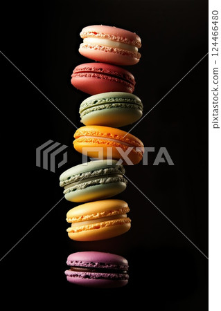 A vertical cascade of macarons in rainbow hues pops against a dark black background 124466480