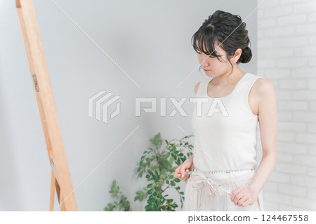 Asian woman measuring her waist in front of a mirror (diet, constriction, size down, three sizes) 124467558