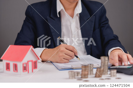 Loan documents and finance agreement on table near home model for ownership planning. Buying or selling a house involves money management and legal agreements for secure deals and insurance 124471504