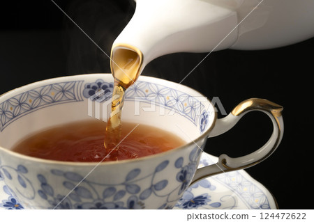 Pouring tea into a teacup with a teapot Pouring tea into a teacup with a teapot 124472622